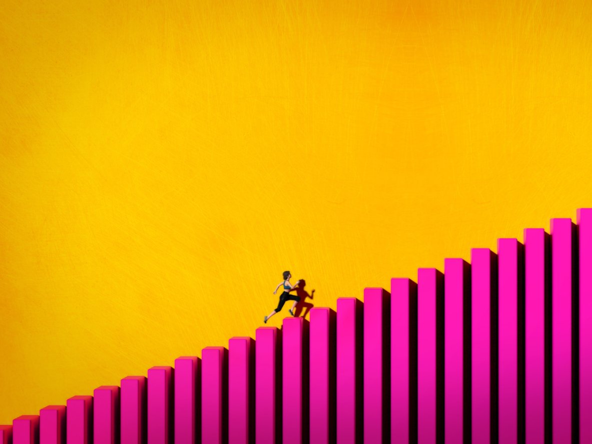 A person running uphill on a ski lift made of pink and purple pillars against a yellow sky